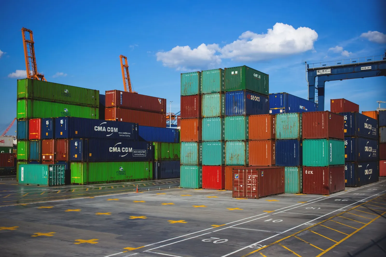 Green, blue and red shipping containers stacked high in a storage yard under a clear sky