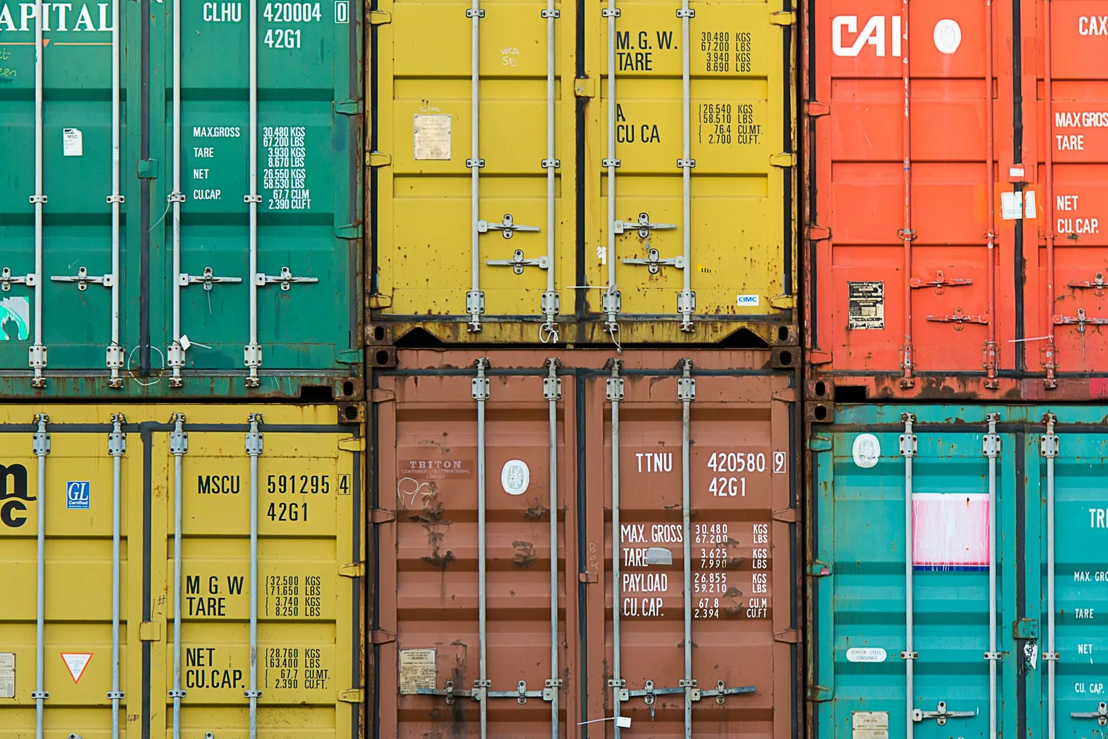 Stacked used shipping containers in green and brown with weathered cargo doors and markings