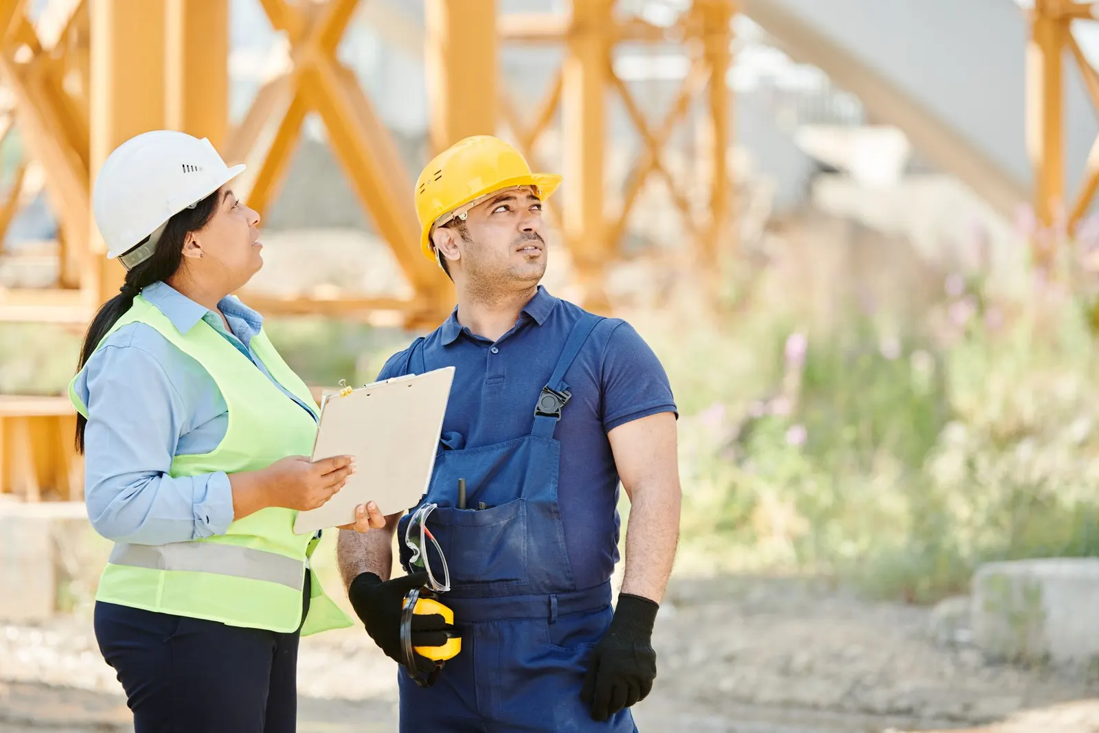 Two engineers in hard hats and hi-vis reviewing plans on site